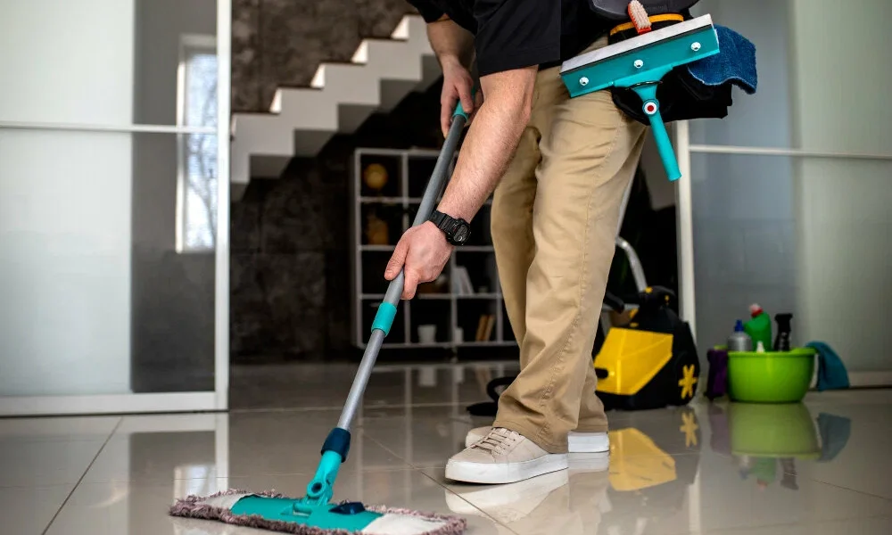 Person mopping shiny tile floor with turquoise mop and cleaning supplies in modern home interior